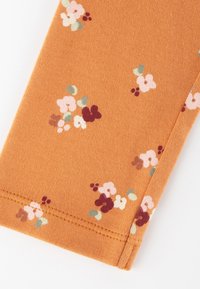 Oranges Stoff mit einer strukturierten Oberfläche, die verstreute Blumenmuster in Pink, Lila und Grün zeigt. Die Nähte sind ordentlich genäht.