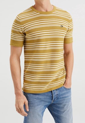 Camiseta amarilla a rayas con líneas horizontales blancas, cuello redondo, mangas cortas, tejido texturizado, combinada con jeans azules. Pequeño logo en el pecho.
