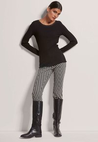 Schwarzes, geripptes Langarmshirt mit Spitzen-Ausschnitt, kombiniert mit leggings in Schwarz-Weiß-Muster und knielangen schwarzen Lederstiefeln.