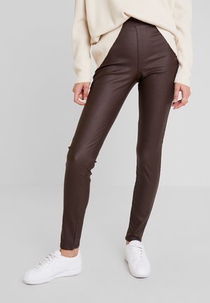 Legginsy zestawione z kremowym swetrem i białymi tenisówkami, stojące na tle gładkiego jasnoszarego tła.