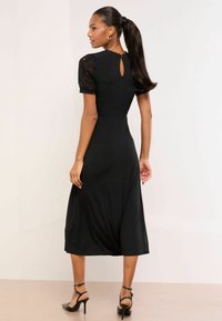 Schwarzes Midikleid mit Spitzenärmeln in Puffärmel-Optik, tailliertem Oberteil, Rückenausschnitt mit Schlüsselloch-Detail und fließendem Rock. Glatte Stoffstruktur und elegantes Design.