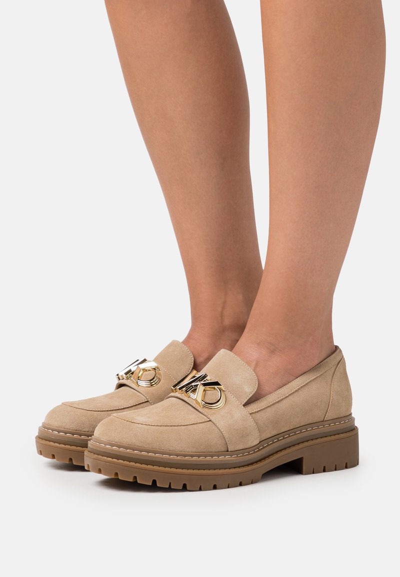 Mocassini in suede beige con suola in gomma spessa, caratterizzati da un vistoso dettaglio in metallo dorato sulla tomaia e cuciture decorative.