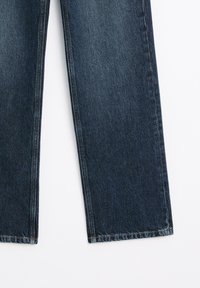 Jean en denim bleu foncé avec jambes droites montré de la moitié de la cuisse jusqu'à l'ourlet sur fond blanc.