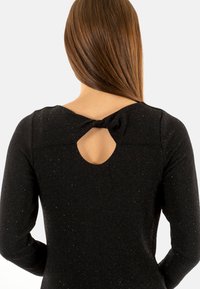 Abito lungo nero a maniche lunghe con una finitura testurizzata e luccicante. Presenta un'apertura a forma di chiave sulla schiena e un dettaglio annodato vicino allo scollo.