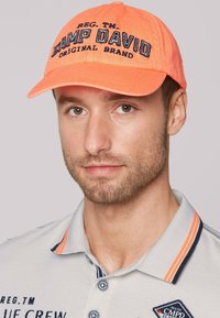 Cappello arancione con "CAMP DAVID ORIGINAL BRAND" ricamato in nero. Tessuto morbido, visiera curva e fascia posteriore regolabile.