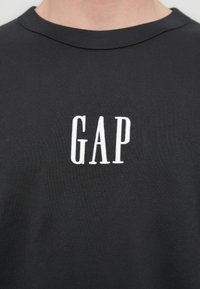 Μαύρο βαμβακερό T-shirt με στρογγυλή λαιμόκοψη. Διαθέτει λευκό κεντημένο λογότυπο "GAP" στο στήθος, απαλή υφή και κλασική εφαρμογή.