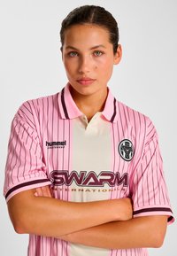 Lyserød og cremefarvet stribet jersey med sorte detaljer, der har krave, logo på brystet og korte ærmer. Glat tekstur og sporty design.