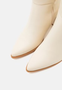 Bottines en cuir blanc avec bouts pointus et texture lisse, dotées d'une fermeture éclair latérale et d'accents de talon beige.