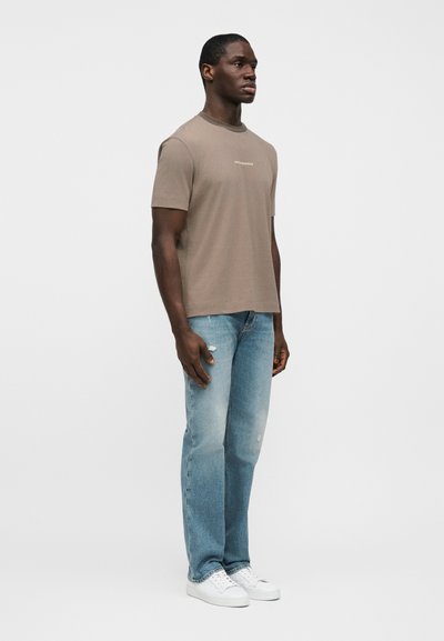 Καφέ κοντομάνικο μπλουζάκι με στρογγυλή λαιμόκοψη, συνδυασμένο με ανοιχτόχρωμα τζιν με φθορές και λευκά αθλητικά παπούτσια. Κανονική εφαρμογή και άνετη σιλουέτα.