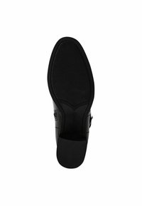 Suela de zapato de cuero negro con una superficie texturizada, forma redondeada y tacón integrado. Presenta un borde liso y un detalle con el logo.