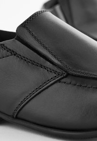 Zapatos de cuero negros con una textura suave, costuras detalladas y un diseño elegante y minimalista. La silueta es de corte bajo y aerodinámica.
