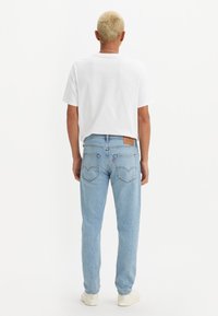 Ljust blå denimjeans med avslappnad passform, utrustade med en brun läderlapp och bakfickor, kombinerade med en enkel vit t-shirt.