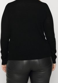 Pull en tricot noir à manches longues avec ourlet côtelé, associé à un pantalon en cuir noir ajusté avec des poches arrière.