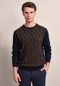 Strickpullover mit einem geometrischen braunen Muster auf einem marineblauen Grund, mit gerippten Bündchen und Saum sowie rundem Halsausschnitt. Weiches Material.