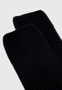 Sorte ribbede sokker lavet af blød stof med en tekstureret overflade. Har en lige kant i toppen og en glat inderside.