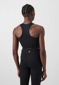 Sustentação preta desportiva com um design de costas nadador, confeccionada em um material ajustado e respirável. Leggings altas pretas com um pequeno detalhe de logotipo.