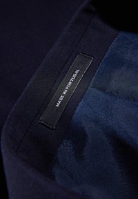Fodera in tessuto blu navy con texture liscia; etichetta nera con la scritta "MADE IN PORTUGAL". Design pulito con hardware minimale e lucentezza sottile.