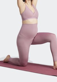 Vaaleanpunainen urheiluliivi ja korkeavyötäröiset legginsit, jotka on valmistettu venyvästä kankaasta. Leggingsit ovat sileäpintaiset ja saumattomat.