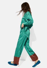 Zielony kombinezon w kropki z długimi rękawami, z brązowymi wzorzystymi mankietami. Uzupełniony niebieskimi płaskimi butami dla kontrastu.