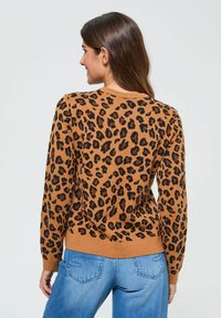 Pull en imprimé léopard en tissu beige avec des taches noires, à col rond et à manches longues. Associé à un jean en denim bleu.