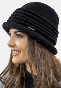 Cappello di lana nero a forma rotonda, con pieghe orizzontali e una texture morbida. Include un dettaglio metallico per dare accentuazione.