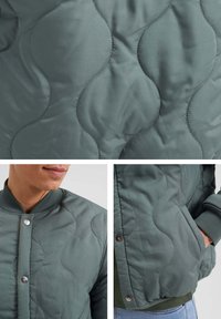 Kudde-bomberjacka i dämpad grön. Har rundade sticksymönster, tryckknappar, ribbade ärmslut och sidofickor. Mjuk, slät textur.