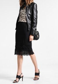 Schwarze Lederjacke, Top mit Leopardenmuster, schwarzer Bleistiftrock mit Spitzenbesatz und schwarze Sandalen mit Absatz. Accessoires umfassen eine kleine schwarze Tasche.