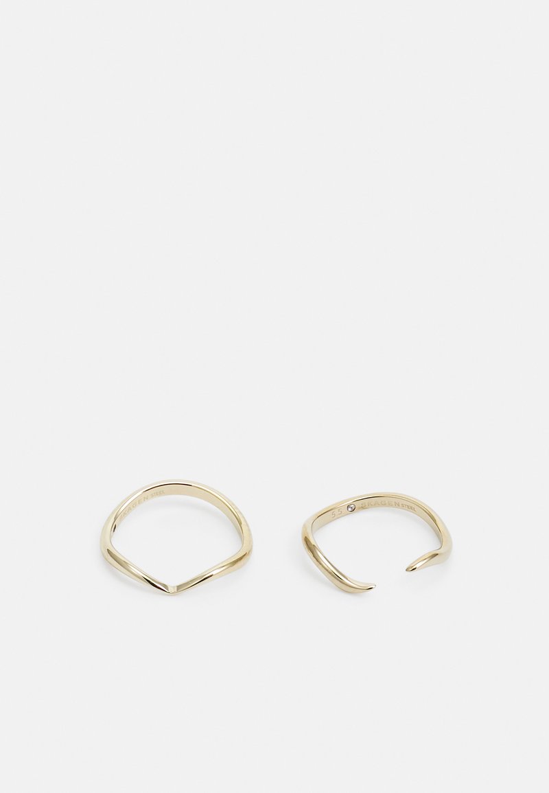 Złocone metalowe pierścienie o gładkim, polerowanym wykończeniu; jeden ma spiczasty kształt v, a drugi otwarty, zakrzywiony design.