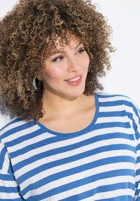 Baumwoll-T-Shirt mit blau-weißen horizontalen Streifen, Rundhalsausschnitt und kurzen Ärmeln. Weicher Stoff und lässige Passform. Silbergraue Creolen sind sichtbar.