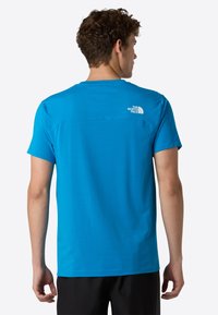 Košile s krátkým rukávem modré barvy vyrobená z lehkého materiálu. Má kulatý výstřih a bílé logo na horní části zad. Jednoduchý design bez vzorů.