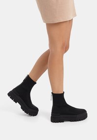 Stivaletti neri alla caviglia realizzati in materiale liscio con una suola spessa e testurizzata. Presentano una chiusura con zip argento sul lato esterno.