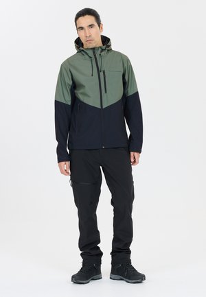Hooded jack met groene bovenkant en marineblauwe onderkant, met ritszakken. Gepaarde met zwarte broek en zwarte wandelschoenen.