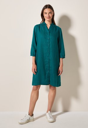Teal linneskjortklänning med knäppning fram, krage och trekvartslånga ärmar. Bärs med vita sneakers. Enkel design och avslappnad passform.