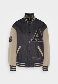 Denim och beige varsityjacka med randiga ribbad muddar, tryckknappar, framfickor och broderad text på bröstet och ärmen.