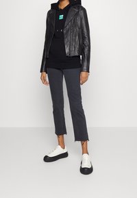 Zwarte leren motorjas over een zwarte hoodie, gecombineerd met grijze cropped broeken en zwart-witte sneakers.