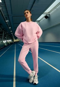 Roosa pusa ja sobivad püksid, valmistatud pehmest kangast, mugava lõikega. Tossud hallide aktsentide ja tekstuurse tallaga.