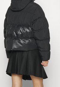 Svart pufferjacka med en glansig textur, oversized passform och huva. Matchad med en veckad svart kjol.