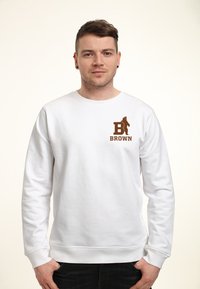 Sweatshirt blanc à manches longues, avec un logo graphique marron sur la poitrine gauche. Tissu doux, poignets et ourlet côtelés. Design simple.