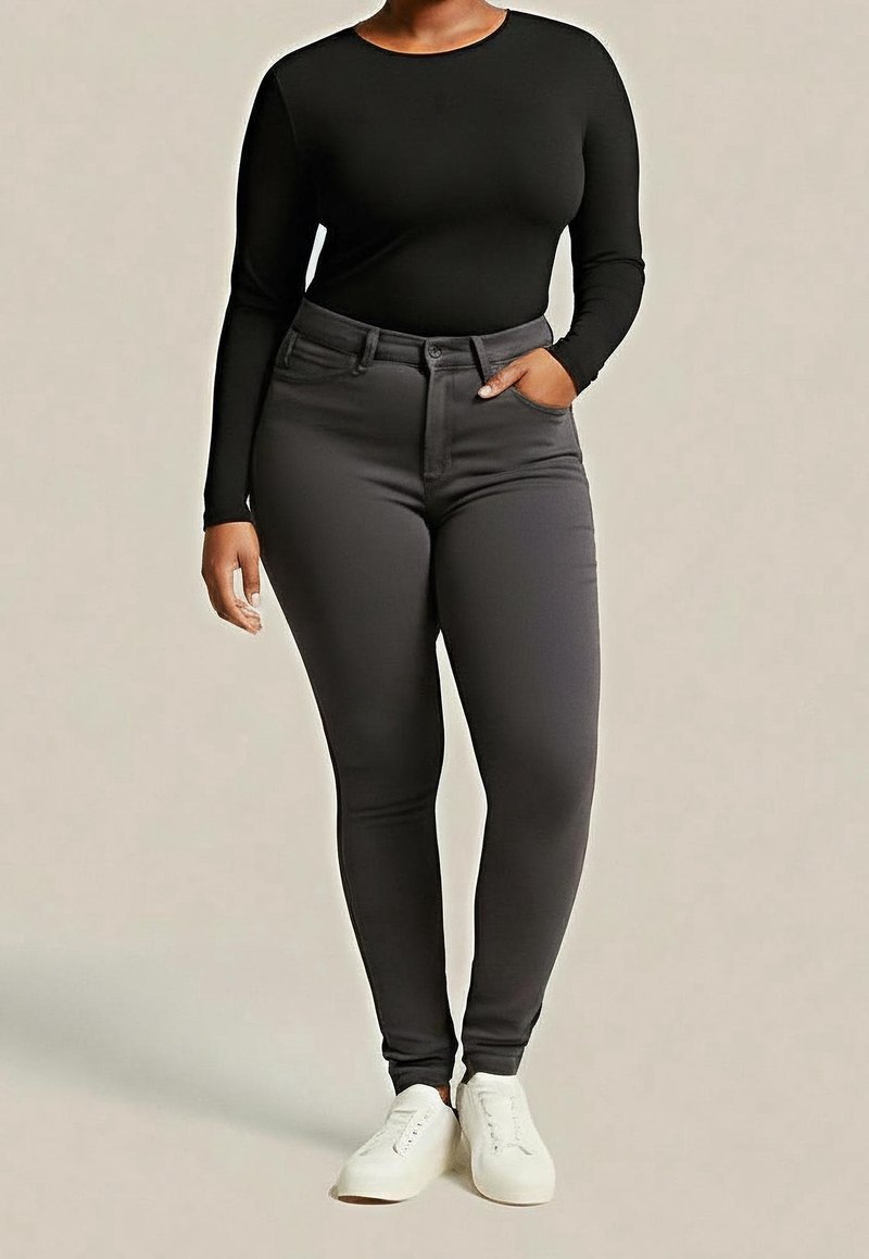 Czarna bluzka z długim rękawem i obcisłe, wysokiej talii ciemnoszare dżinsy o gładkiej fakturze materiału i minimalistycznym kroju. Całość dopełniają białe trampki.