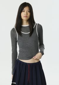 Grauer Langarm-Oberteil mit weißen Abschlussdetails, figurbetontem Design und weicher Textur, kombiniert mit einem marineblauen Rock mit Kordelzug und Falten.