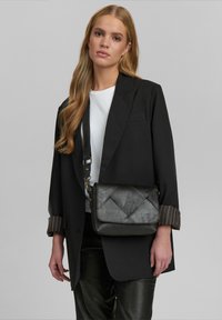 Svart läder crossbody-väska med en kviltad design, flikstängning, justerbar rem och detaljer i guldfärgad metall.