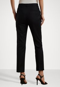 Black tailored trousers with a slim fit, featuring back pockets and a straight leg design. Paired with black strappy high-heeled sandals.