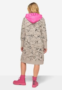 Abito maglione beige con cappuccio, decorato con motivi di pesci neri, polsini e orlo a costine. Cappuccio rosa acceso con dettagli del logo. Abbinato a stivaletti rosa.