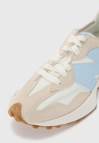 Beige und hellblaue Sneaker aus einer Kombination von Veloursleder und Mesh-Material, mit rundem Zehenbereich, dicker Sohle und weißen Schnürsenkeln. Texturierte Akzente sind sichtbar.