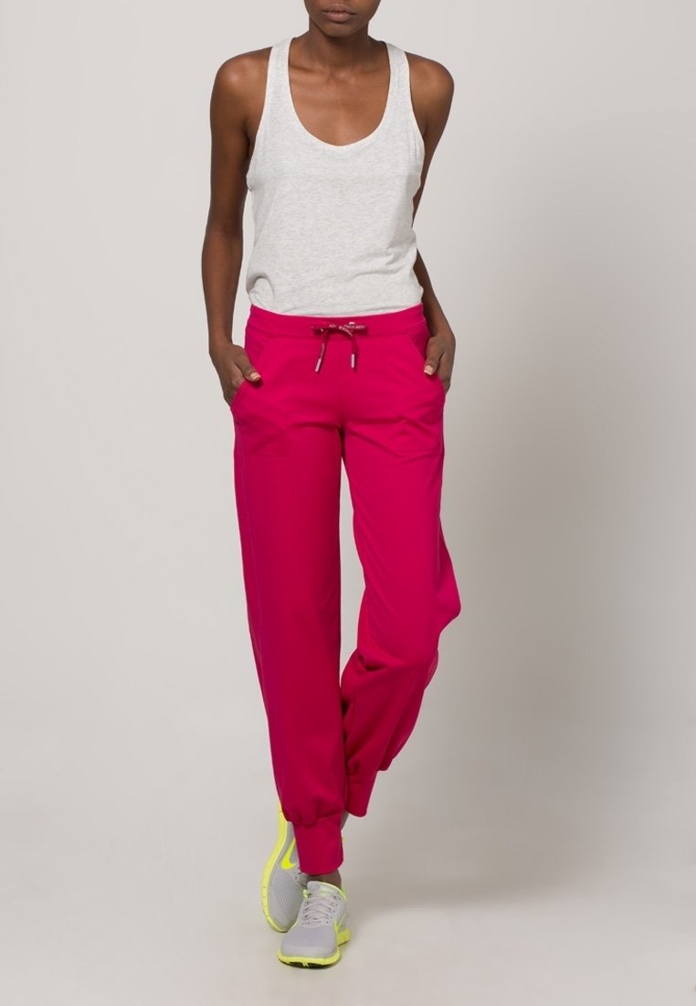 Roze joggerbroek met een trekkoord in de taille en zijzakken, gecombineerd met een lichtgrijs tanktop en grijze sportschoenen met neonaccenten.