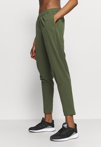 Green athletic pants with an elastic waistband, side pockets, and a tapered design, paired with black running shoes featuring a white sole.