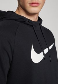 Sweat à capuche noir avec un logo Nike Swoosh blanc, doté d'une capuche ajustable par cordon et d'un tissu texturé. Vue rapprochée mettant en avant l'encolure et la couture de l'épaule.