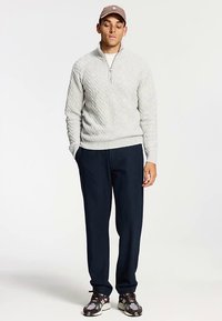 Jersey de punto gris claro con cremallera de cuarto de largo, con un patrón de chevron. Combinado con pantalones de vestir azul oscuro y zapatillas multicolores.