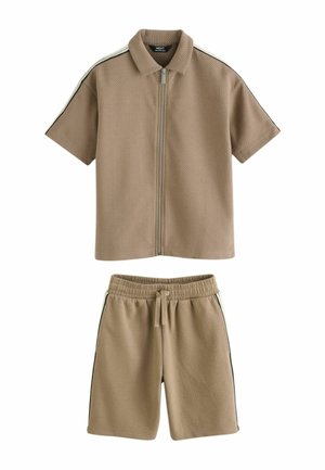Beżowa koszula na krótki rękaw z zamkiem błyskawicznym, kołnierzykiem oraz dopasowane szorty z elastycznym pasem, oba z czarno-białymi paskami po bokach.