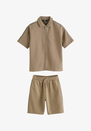 Chemise beige à manches courtes avec fermeture éclair et col, short assorti à taille élastique, tous deux ornés de bandes latérales noires et blanches.